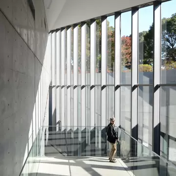 A man on a staircase with floor-to-ceiling windows inside a museum in Tokyo.