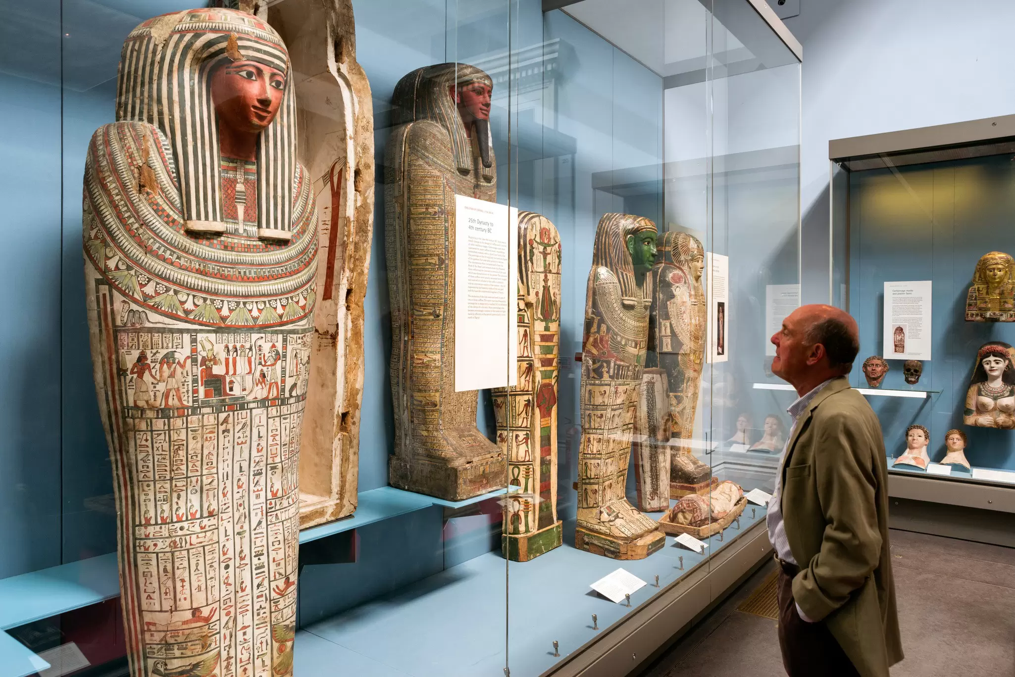 A set of Egyptian artefacts in a display case in a museum. An older white man in a suit is admiring them.