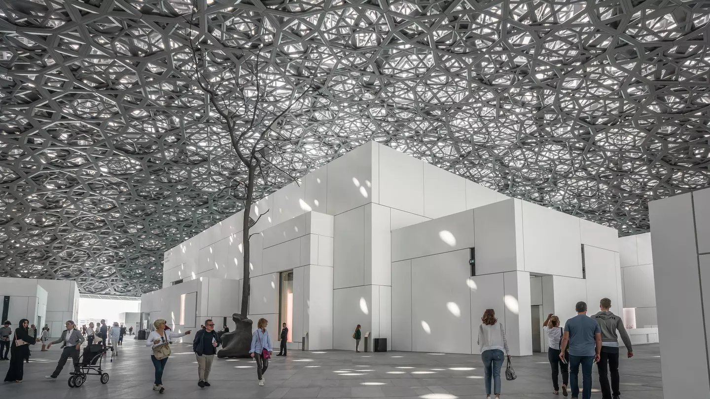 A monumental dome made of latticed metal lets in light to cube-shaped galleries below, with people milling underneath