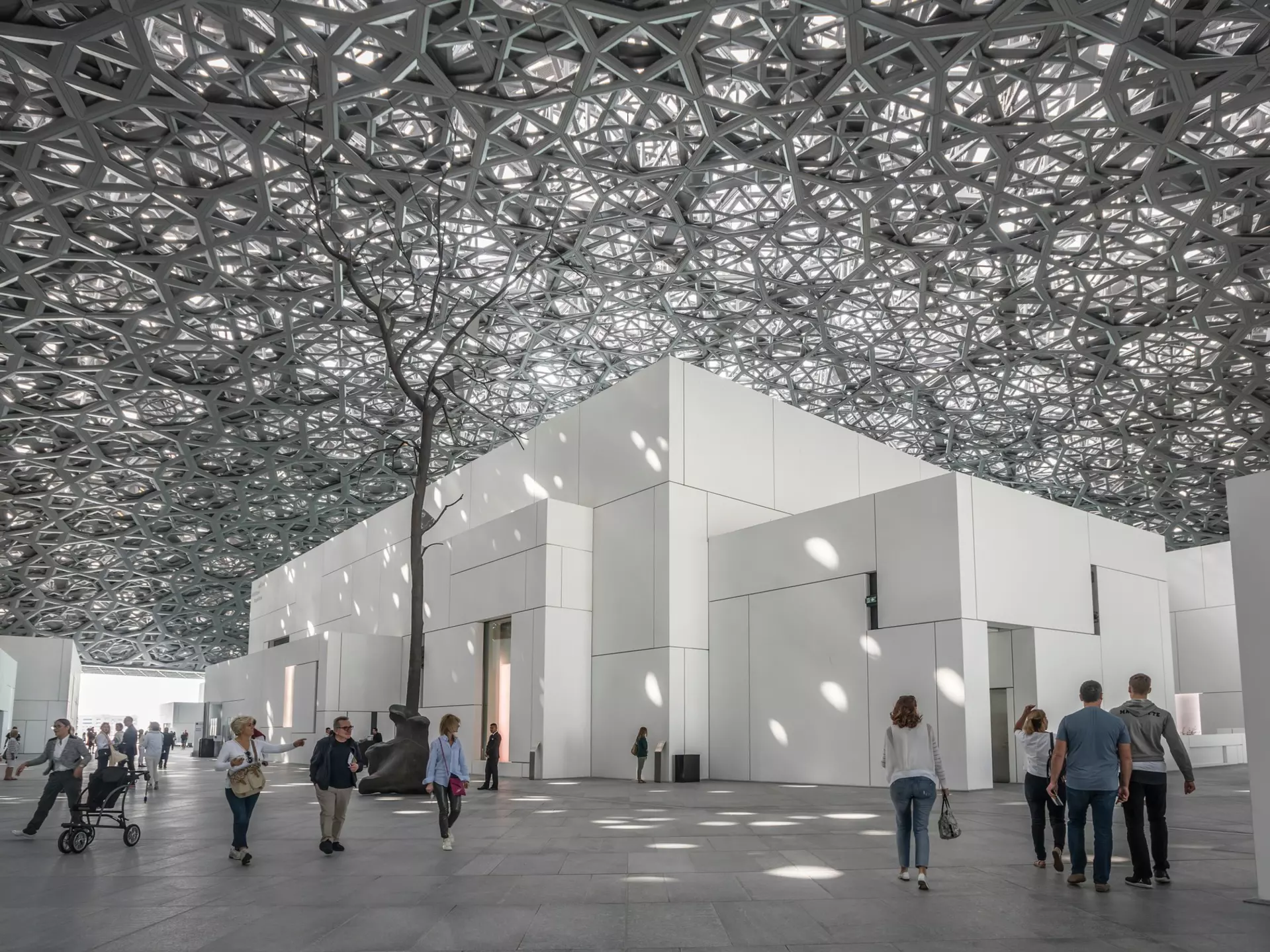 A monumental dome made of latticed metal lets in light to cube-shaped galleries below, with people milling underneath