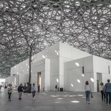 A monumental dome made of latticed metal lets in light to cube-shaped galleries below, with people milling underneath