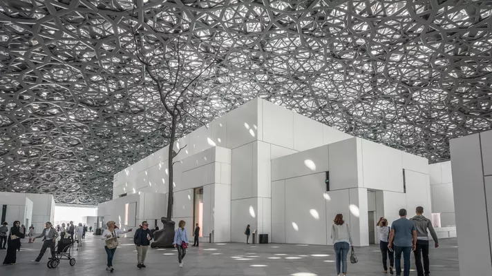 A monumental dome made of latticed metal lets in light to cube-shaped galleries below, with people milling underneath