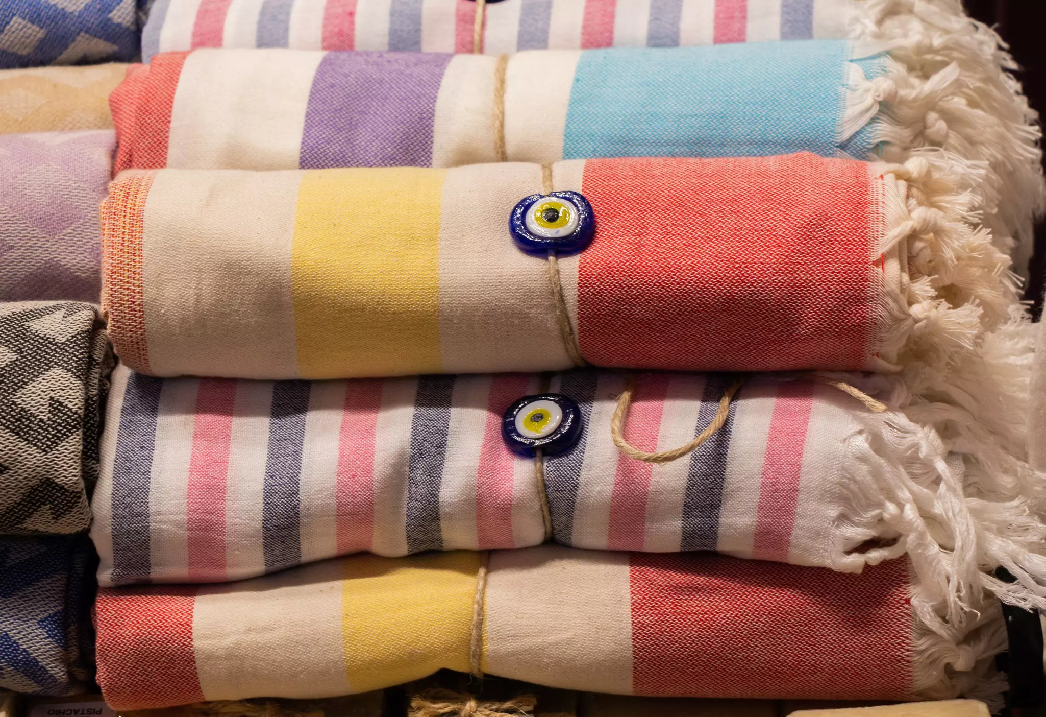 Striped colorful cotton sheets with tassels stacked in a pile at a market stall.