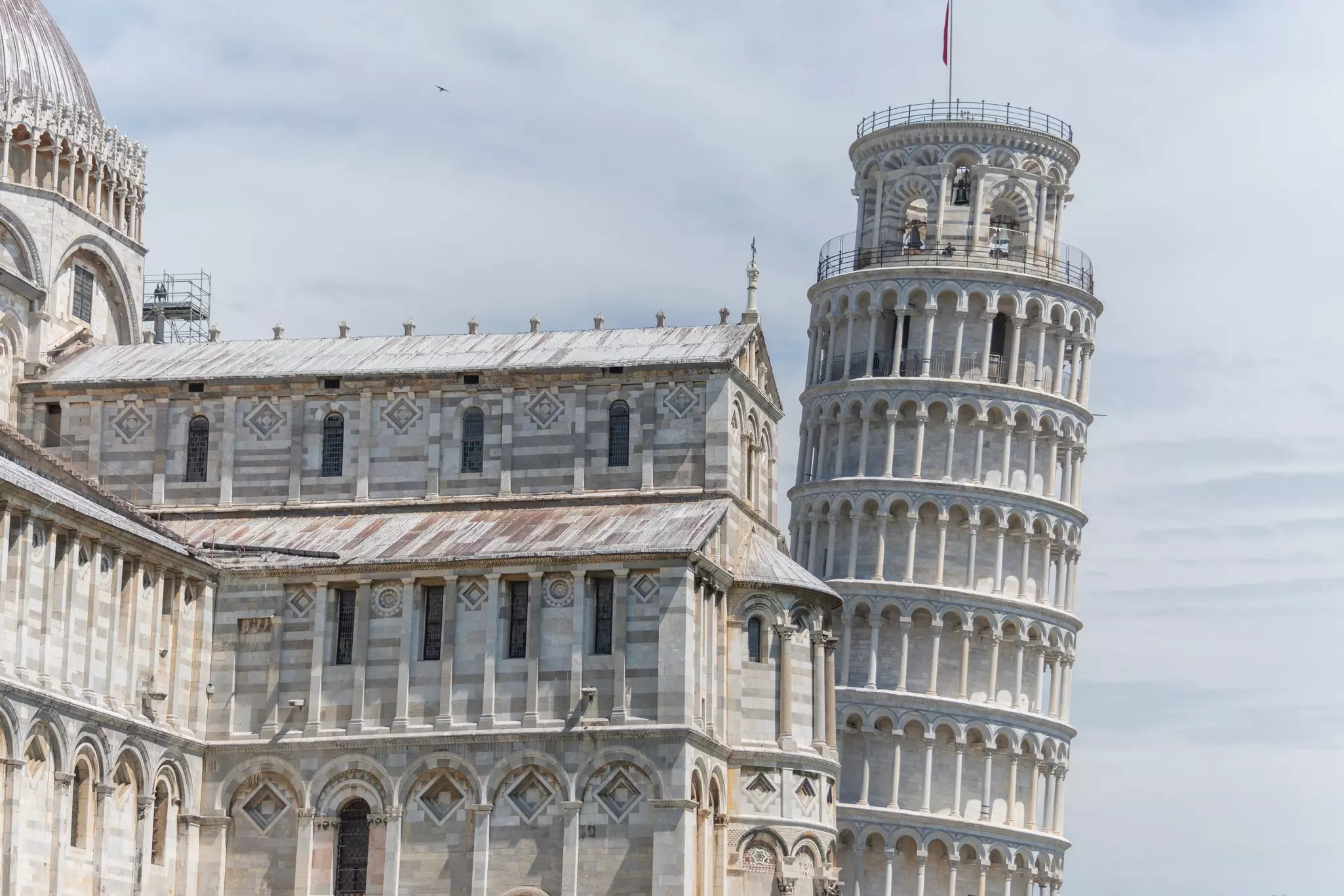 A vast marble cathedral building adjacent to a round tower that leans at an angle.