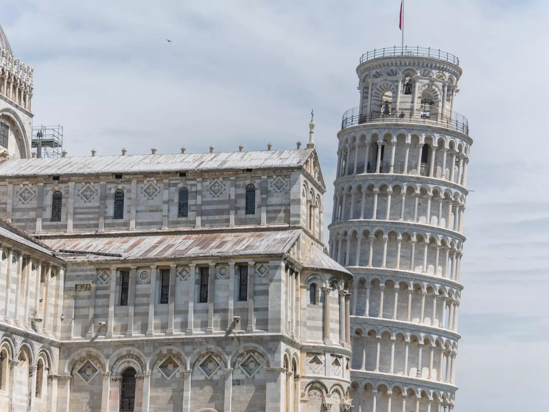 A vast marble cathedral building adjacent to a round tower that leans at an angle.