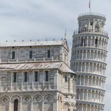A vast marble cathedral building adjacent to a round tower that leans at an angle.