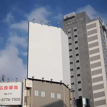 Tall, gray building with the words "Hotel Tokyu Stay" on it, rising into a blue sky