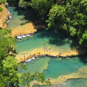 People on narrow strips of limestone between blue pools of water with dense greenery on either side.