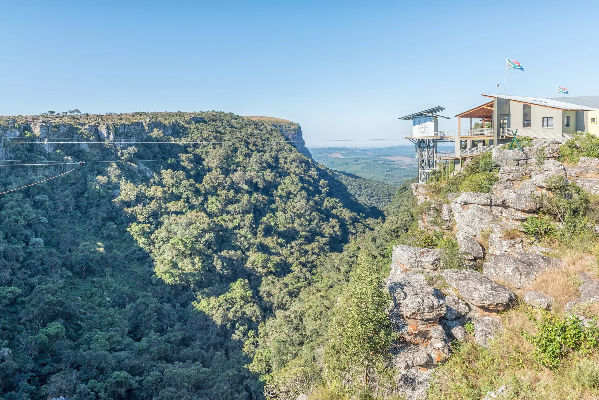 A clifftop structure with a large lift shaft plunging down into a gorge covered in thick vegetation.