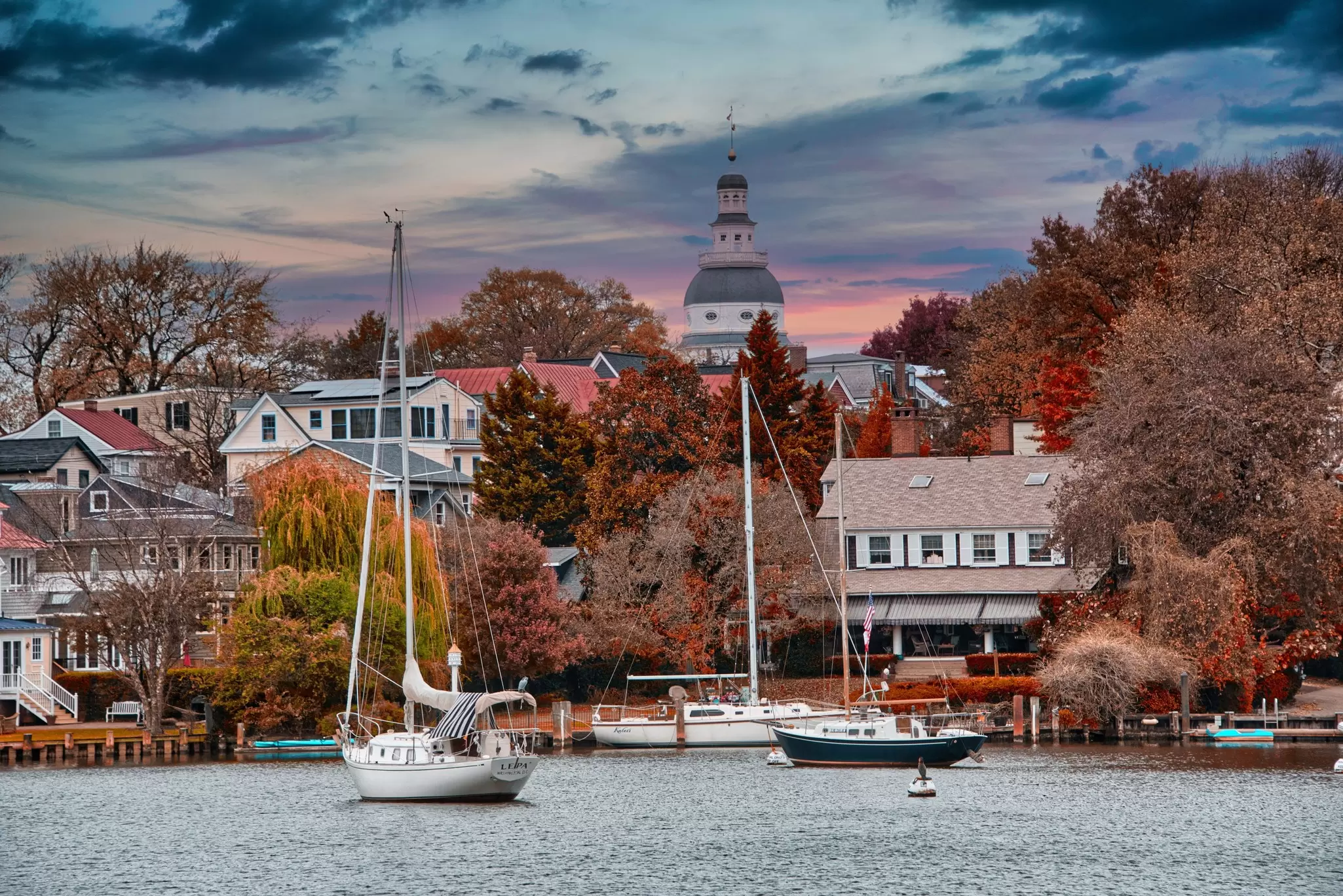 A waterside cove lined with colonial homes and the state capitol building in the background with fall foliage in Annapolis, MD.