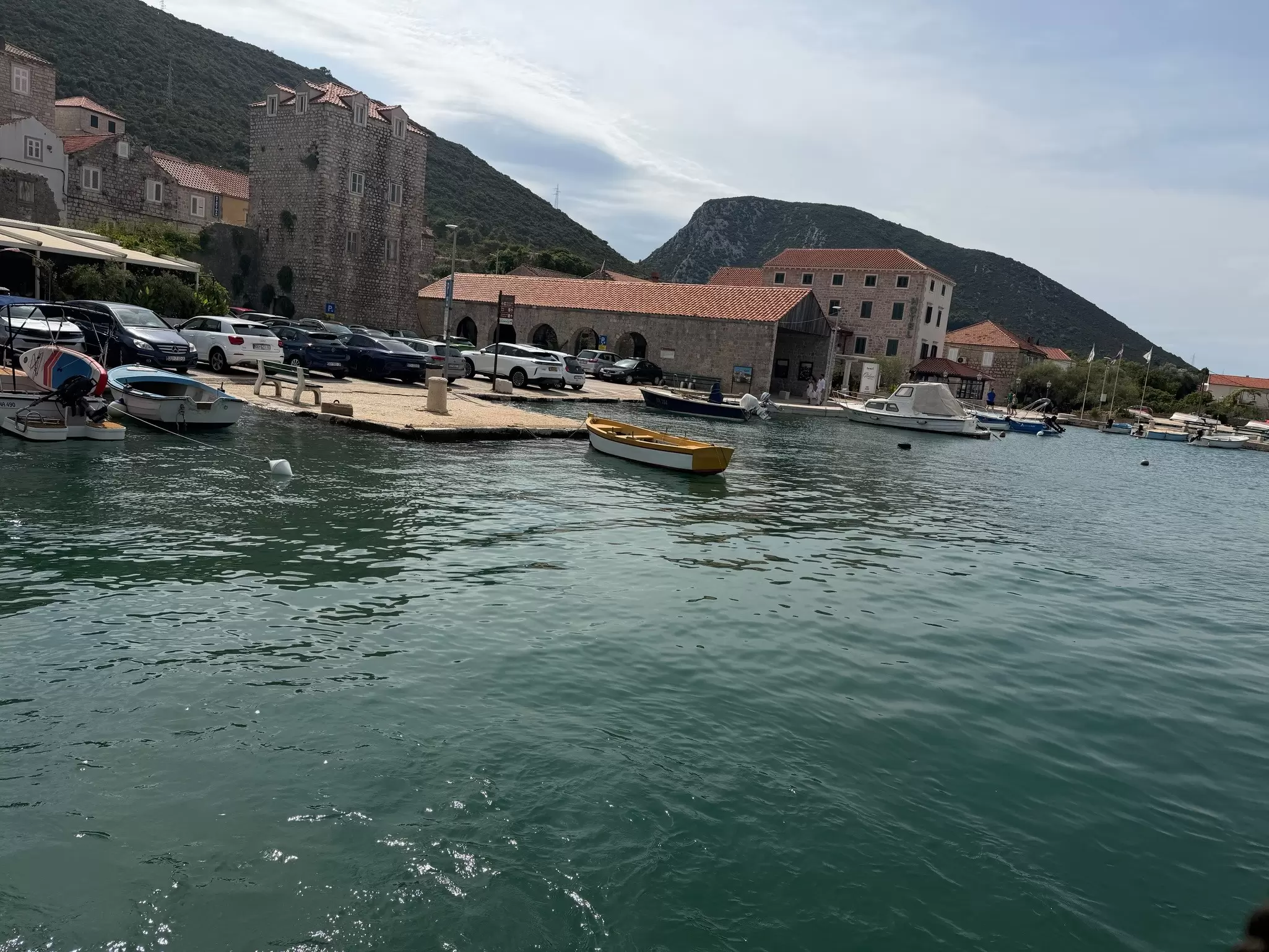 Image of the water with a few boats moored near the shore. In the background there a collection of small buildings. 