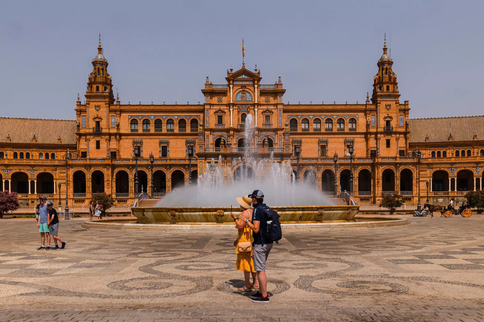 A couple holding a cell phone stand near a fountain in a city square