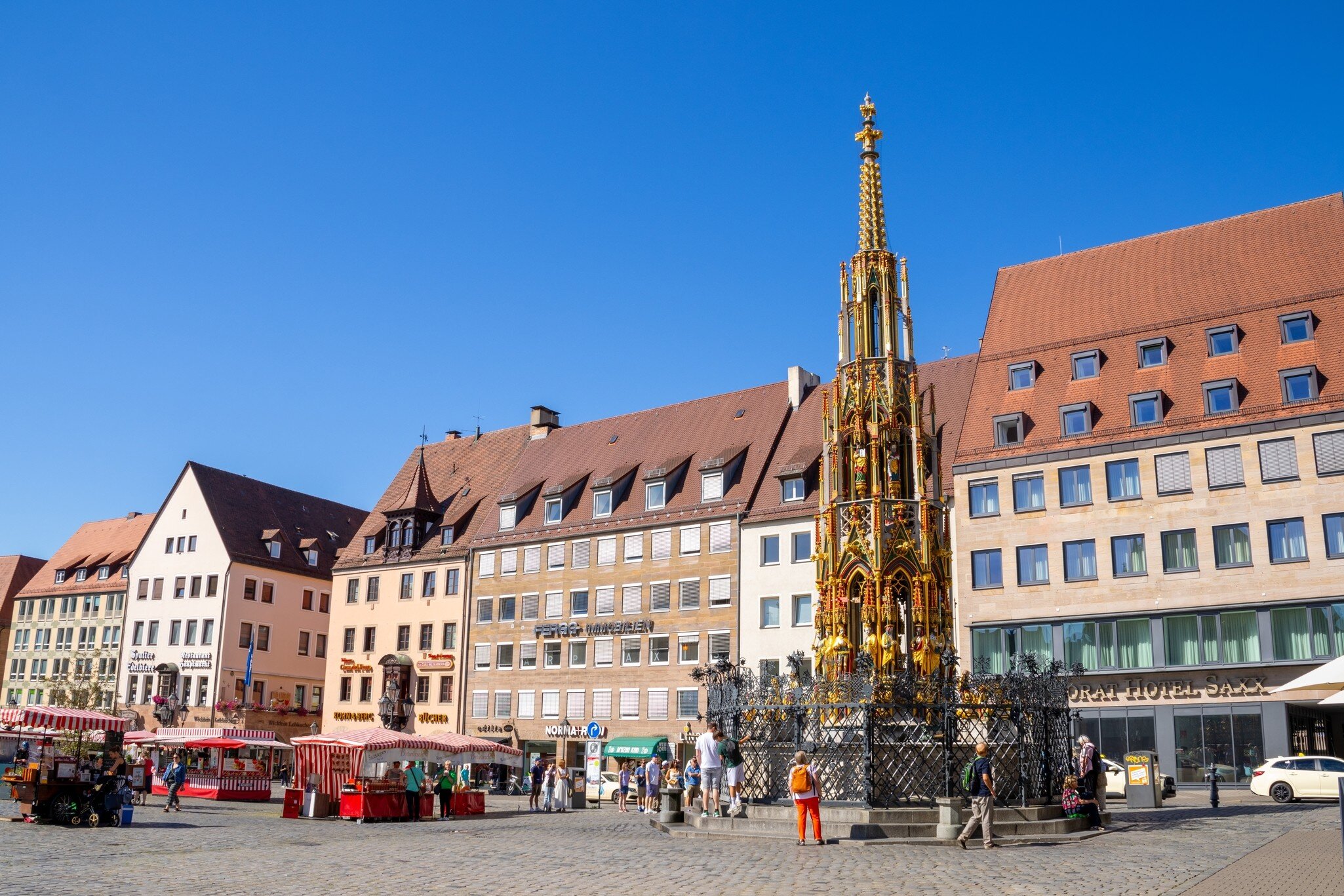 Hauptmarkt in Nuremberg, featuring the Schöner Brunnen fountain and the twin towers of St. Sebald Church, a vibrant historic square under bright daylight. Nuremberg, Germany.