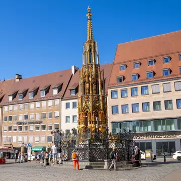 Hauptmarkt in Nuremberg, featuring the Schöner Brunnen fountain and the twin towers of St. Sebald Church, a vibrant historic square under bright daylight. Nuremberg, Germany.