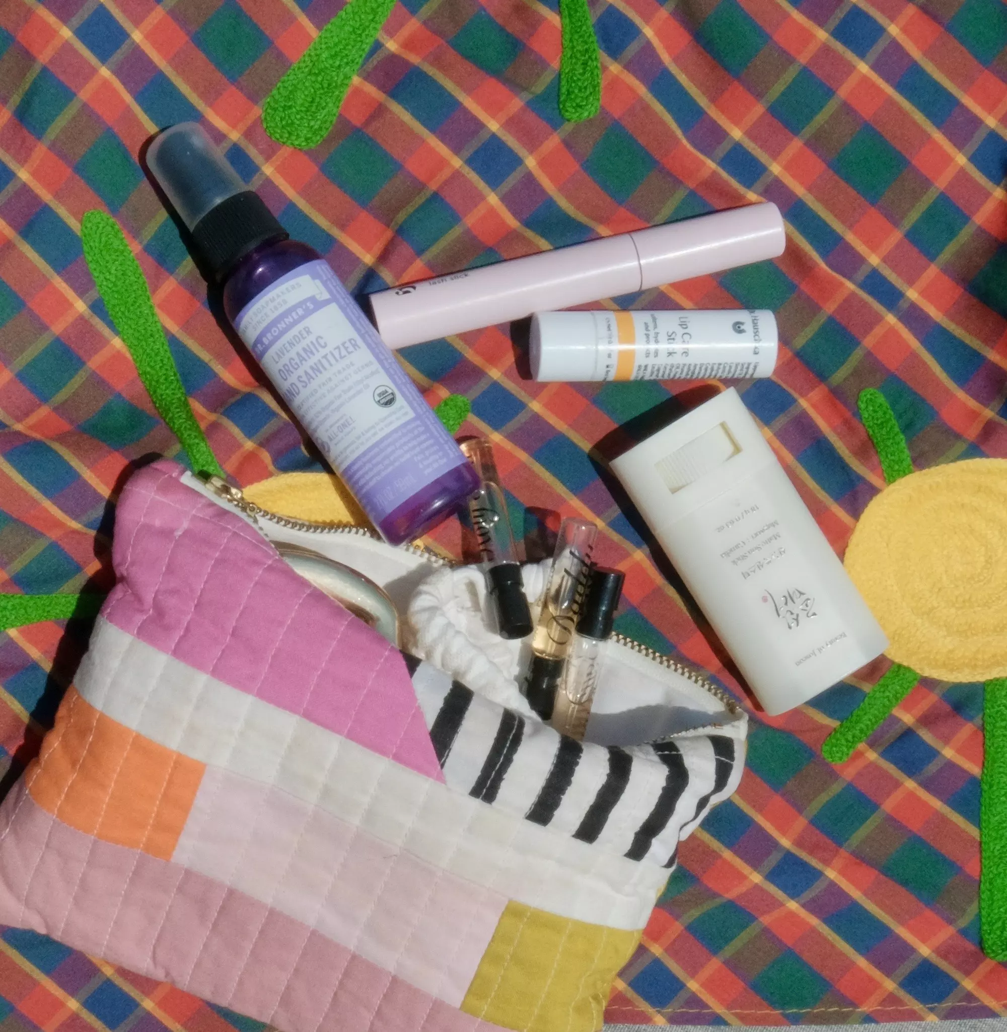 A makeup bag overflowing with mini perfumes, sunscreen and other beauty items is laid out on a check cloth.