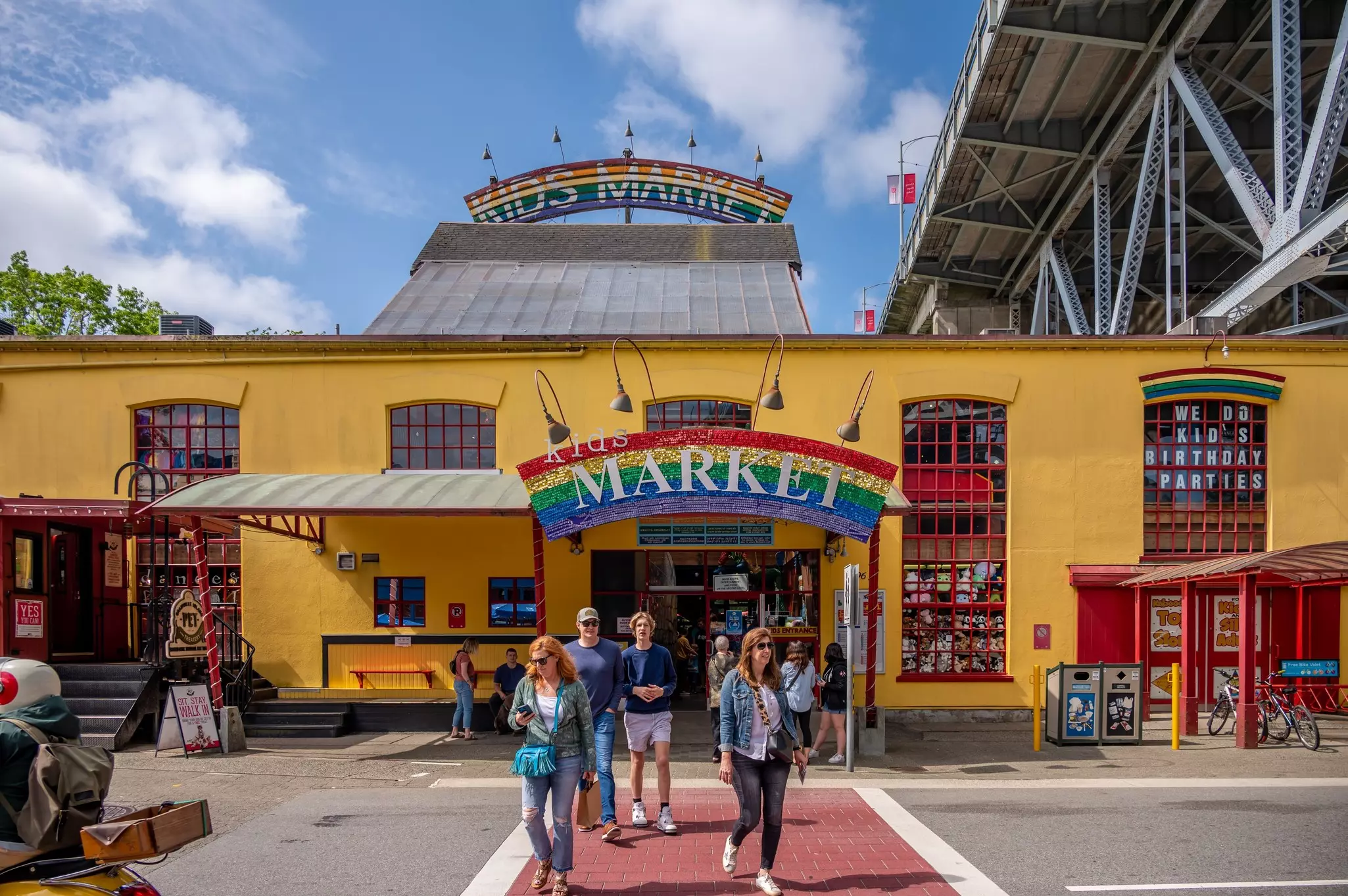 People in front of a yellow building with rainbow sign reading "Kids Market."