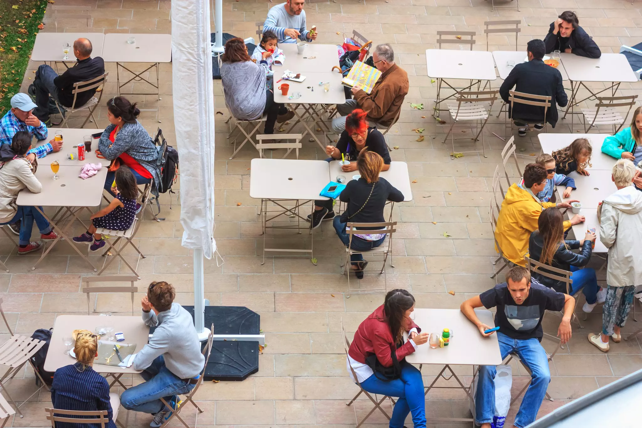 An aerial shot of people sitting at outdoor tables in a city square, enjoying food and drinks.