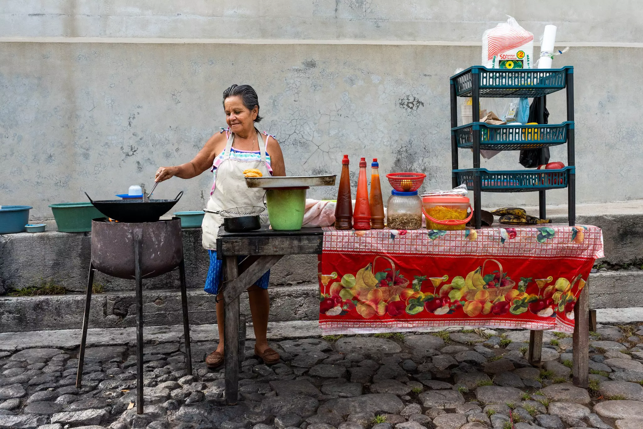 A female vendor in an apron cooking food at a streetside table