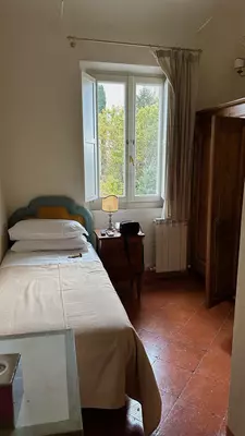 A single bed in a simple narrow room with a window.