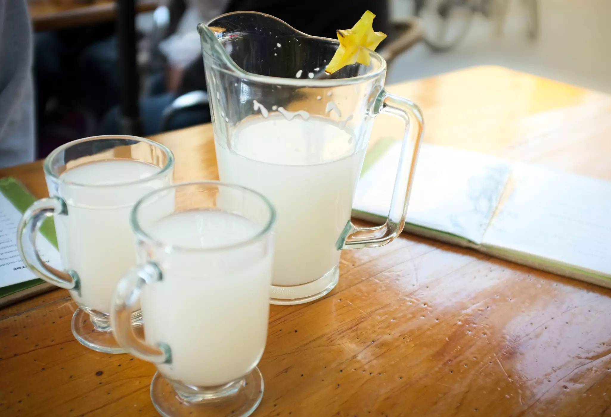 A clear glass pitcher with a handle and two clear handled glasses with a milky liquid.
