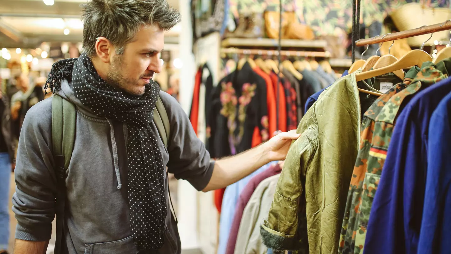 A white man browses through a clothes rail in a second-hand market