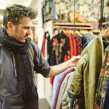 A white man browses through a clothes rail in a second-hand market