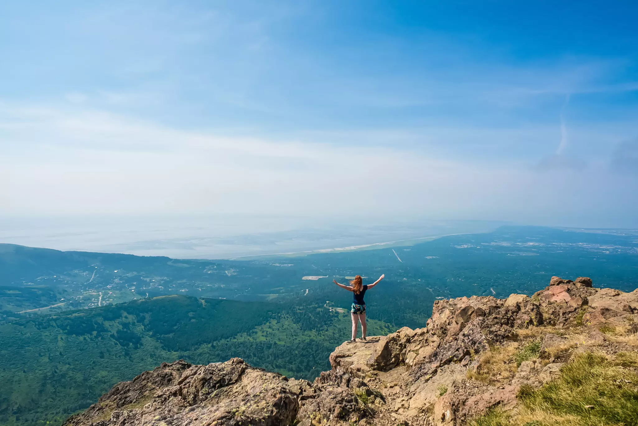 A wide view of a female hiker spreading her arms at a rocky overlook on a mountain.
