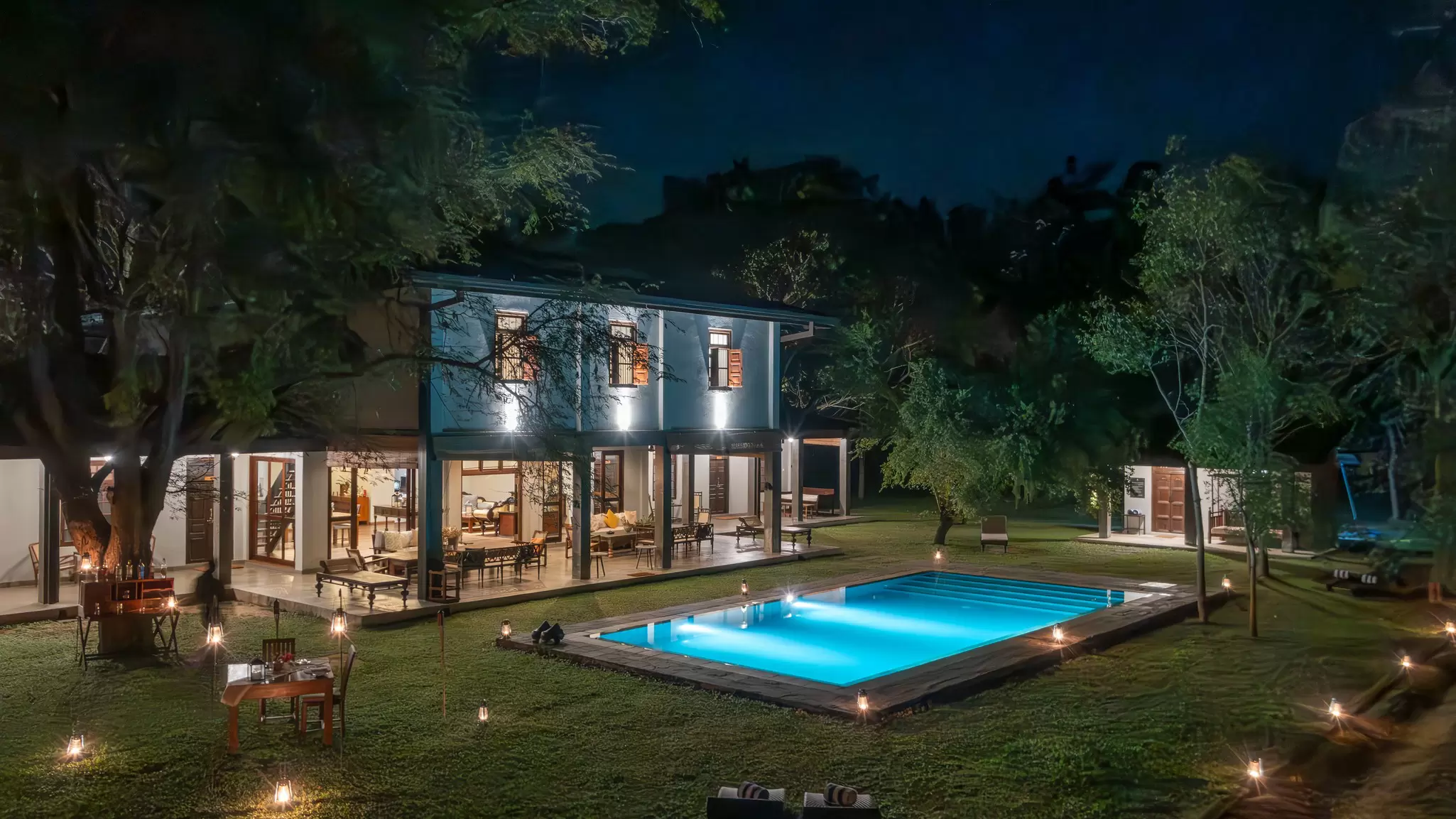 A swimming pool is lit up at night with a safari lodge in the background: the Warden's Lodge, Sri Lanka
