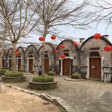 A row of grey stone houses with curved gables and wooden doors, red lanterns strung between bare trees along a cobbled lane.