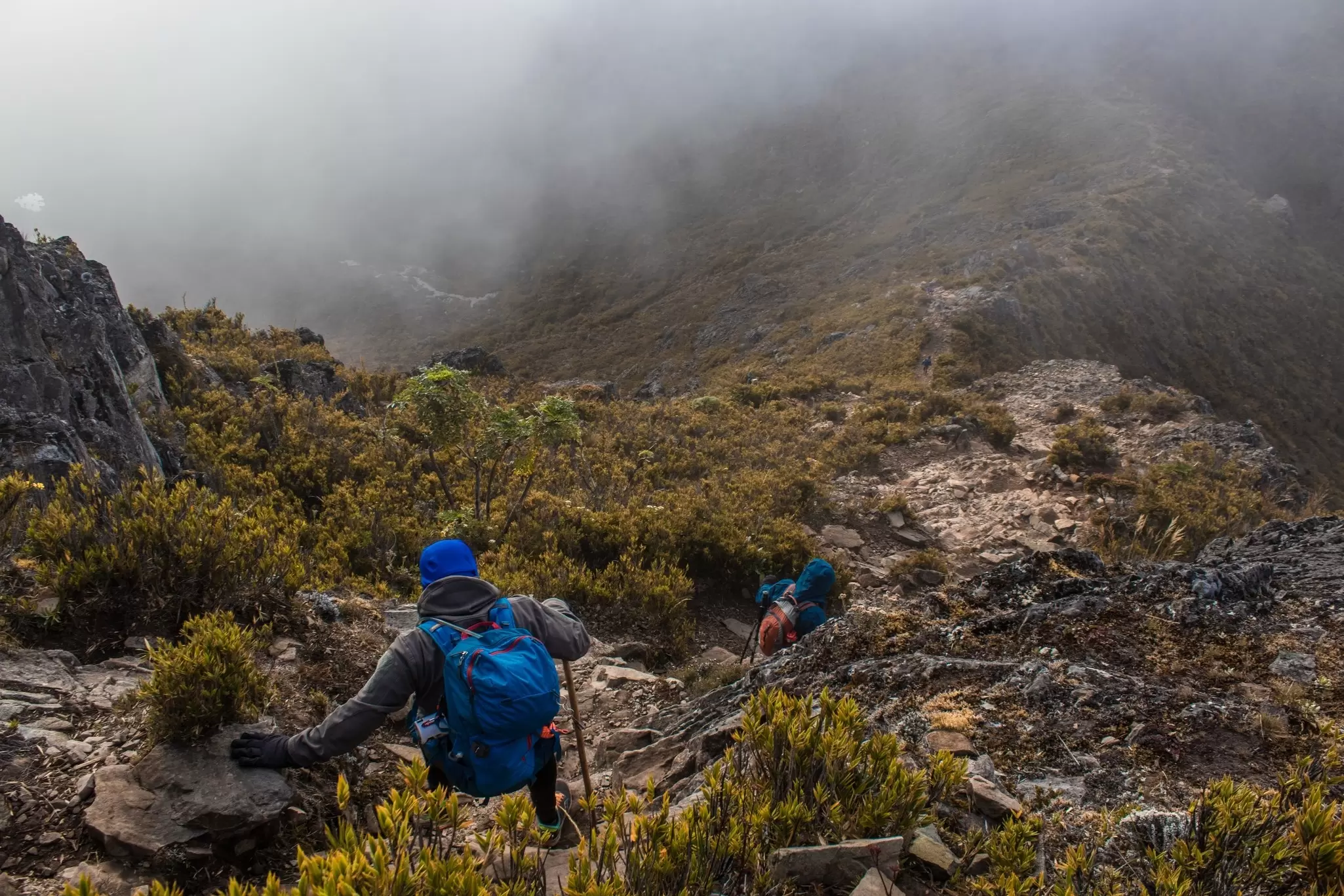 Two hikers descending the rocky mountain with mist clouds on top of Cerro Chirripo in Chirripo National Park in Costa Rica.