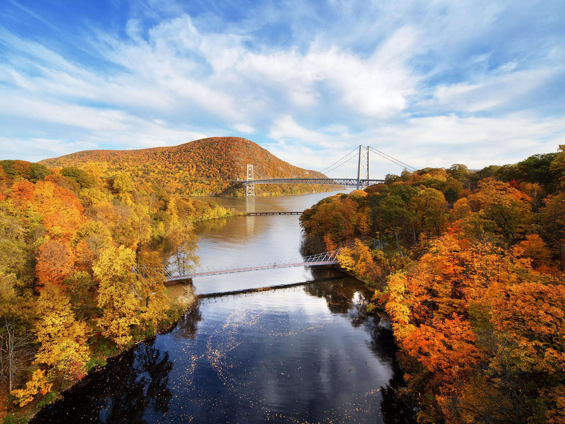 A river winds through lush fall foliage with a bridge in the distance