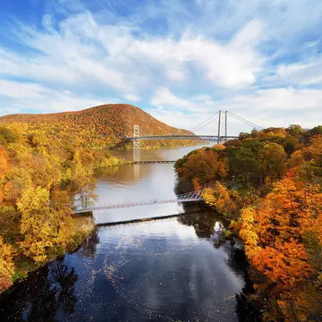 A river winds through lush fall foliage with a bridge in the distance