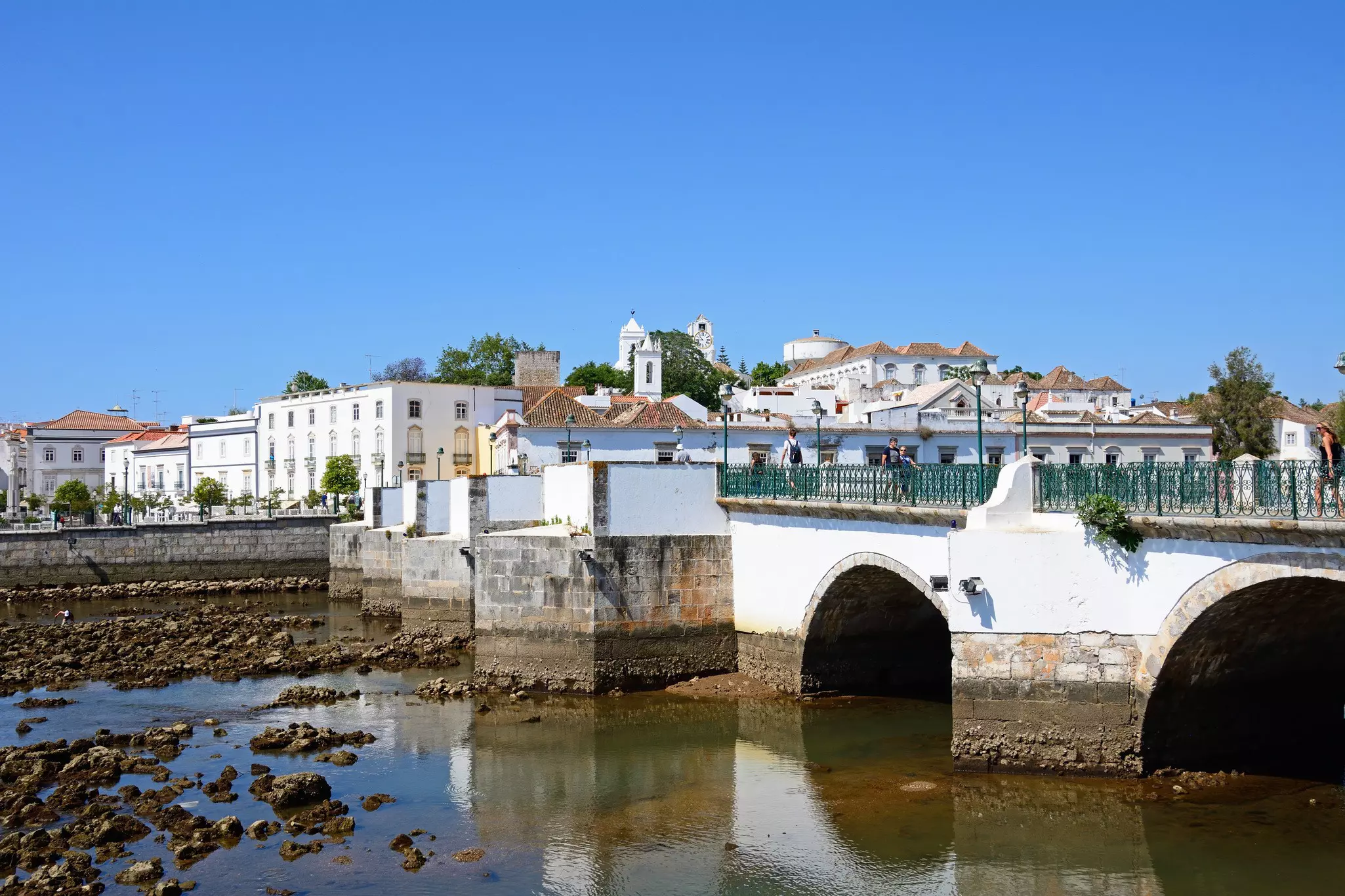 A white bridge over shallow water with white buildings in the background