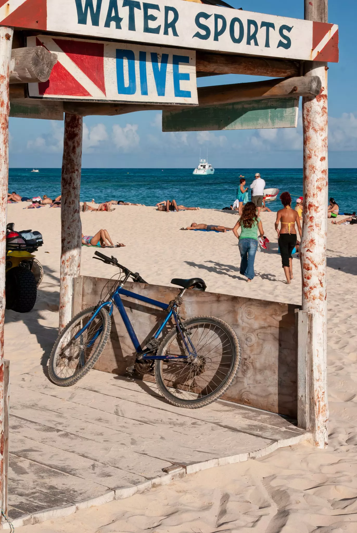 A rustic wooden beach hut with with a bicycle, wooden signs with 'water sport' and 'dive' written on the public beach in Playa del Carmen, Mexico