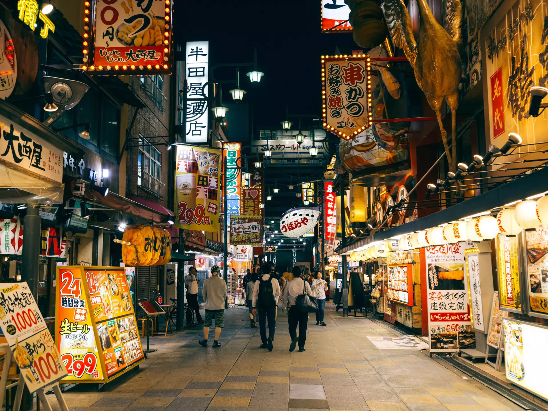 Brightly lit restaurants at night lining a street in the Shinsekai district of Osaka.