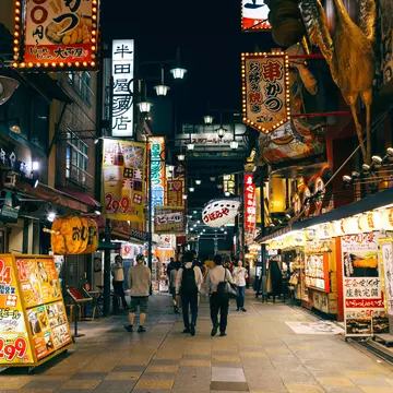 Brightly lit restaurants at night lining a street in the Shinsekai district of Osaka.