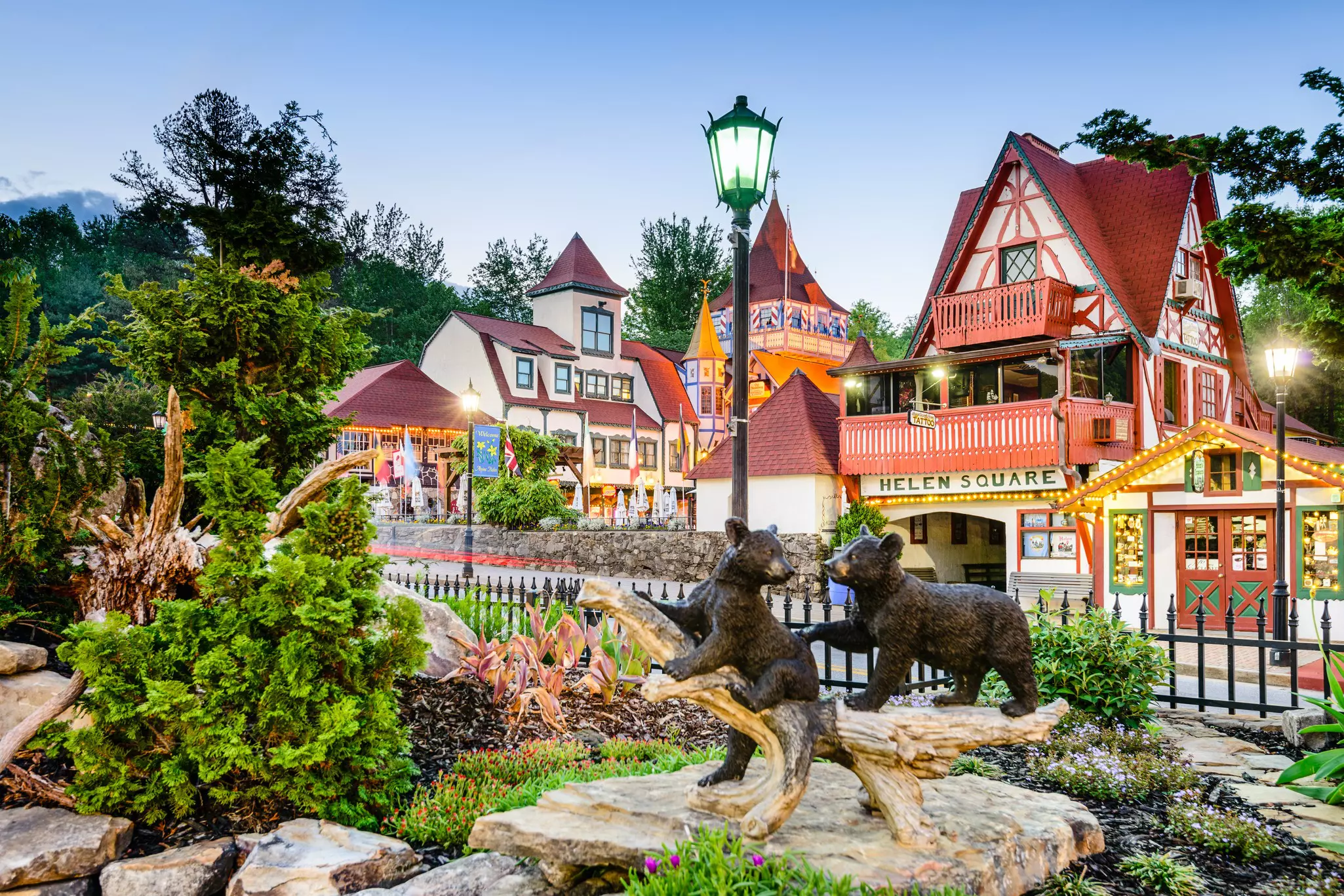 German-style half-timbered buildings form a square in a mountain town. A sculpture of bear cubs is seen in the foreground of the image.