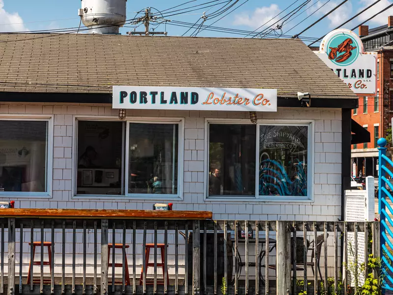 Shingle-sided building with sliding windows and a sign reading "Portland Lobster Co." on a sunny day.