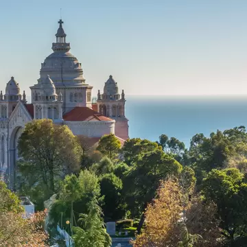 Domed basilica rising above green and autumn trees, a river-mouth beach and calm sea behind, Viana do Castelo.
