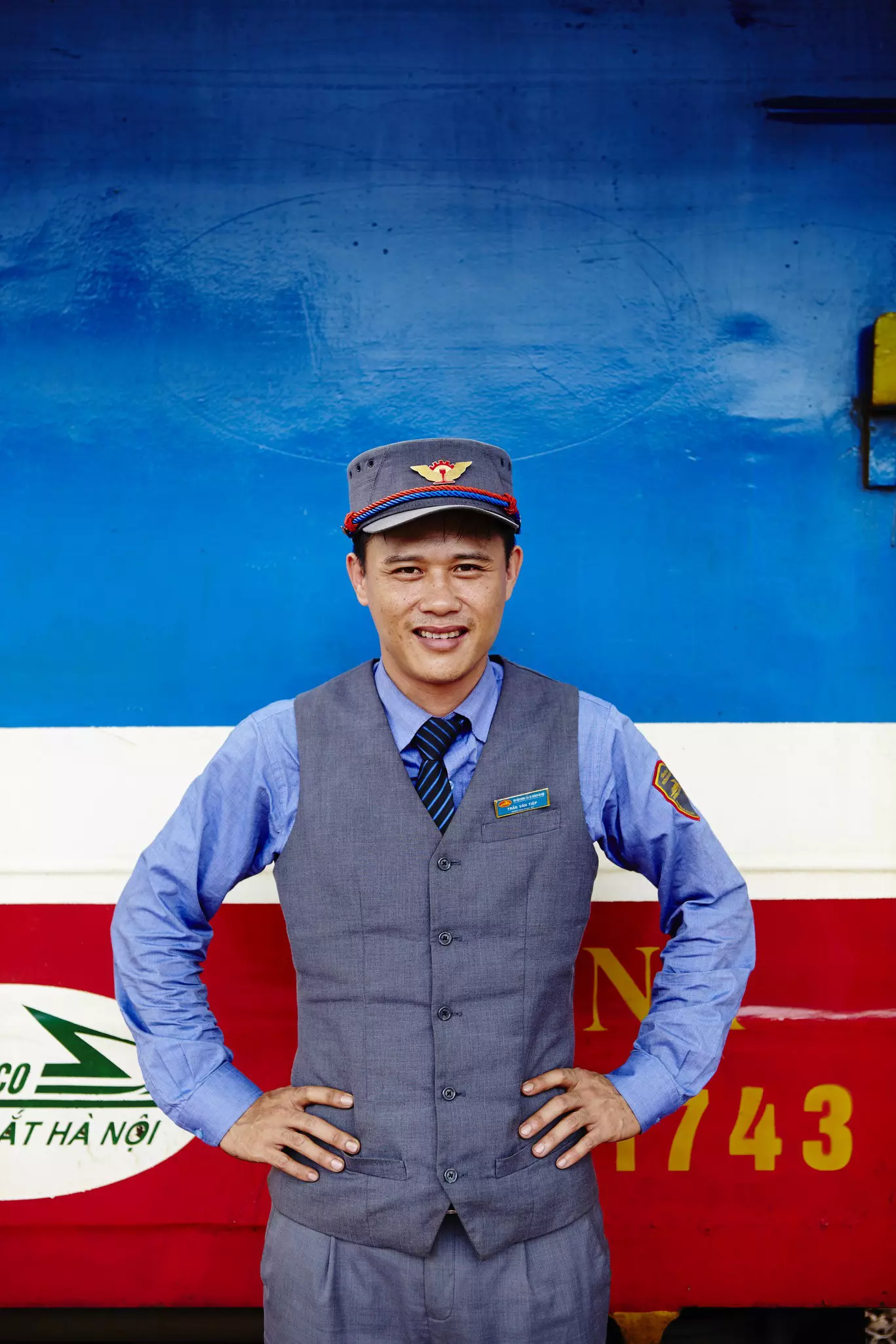 A railway guard standing in front of a red, white, and blue train.