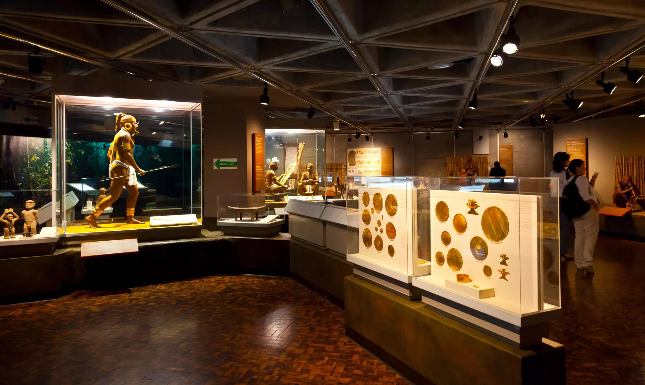 A museum gallery displays gold objects in cases, as well as life-size dioramas of Indigenous people.