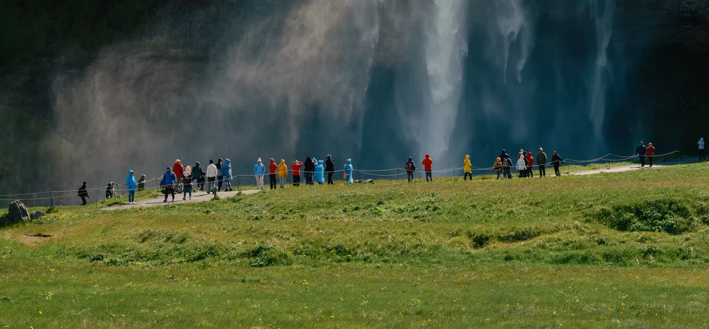 A waterfall in green hills with people below watching 