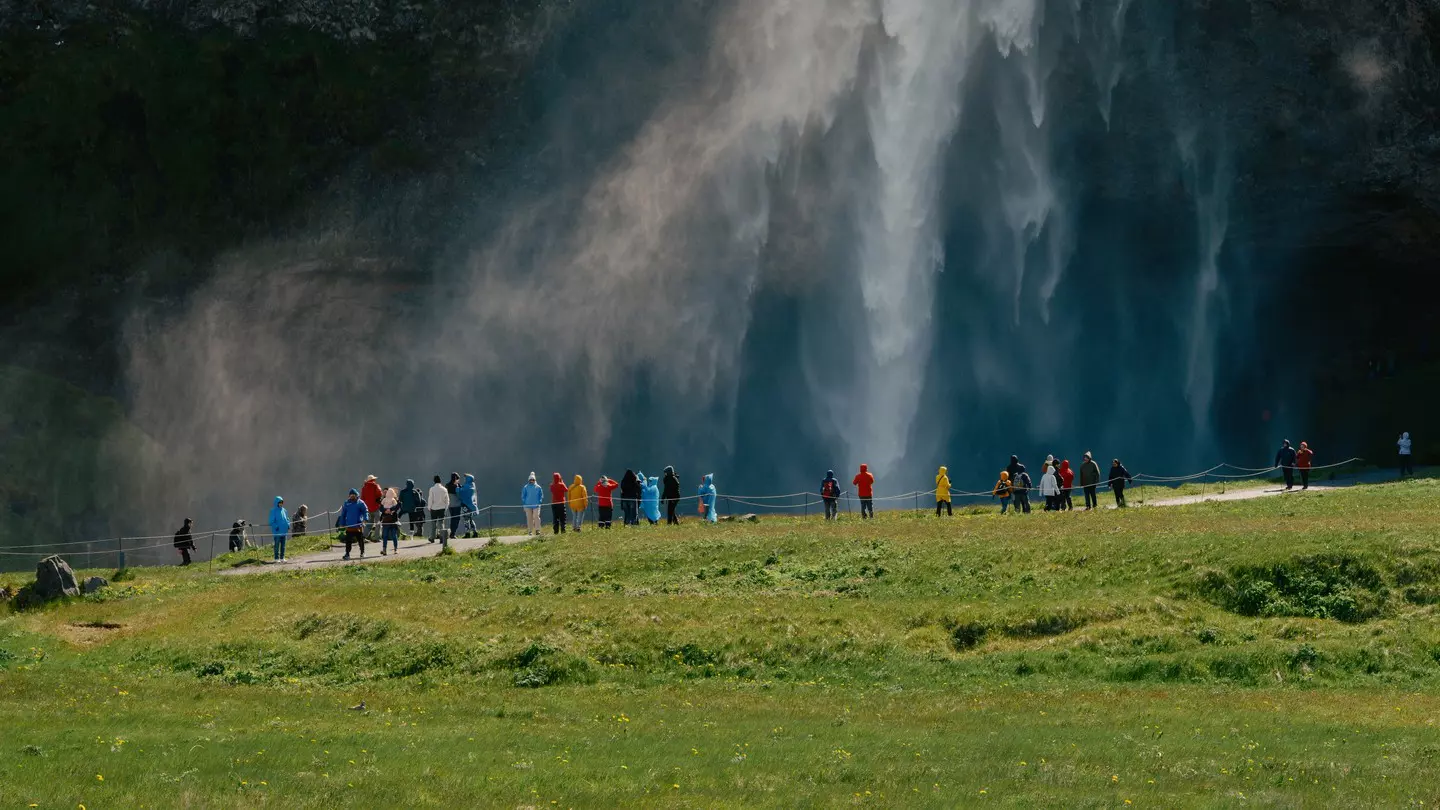 A waterfall in green hills with people below watching 