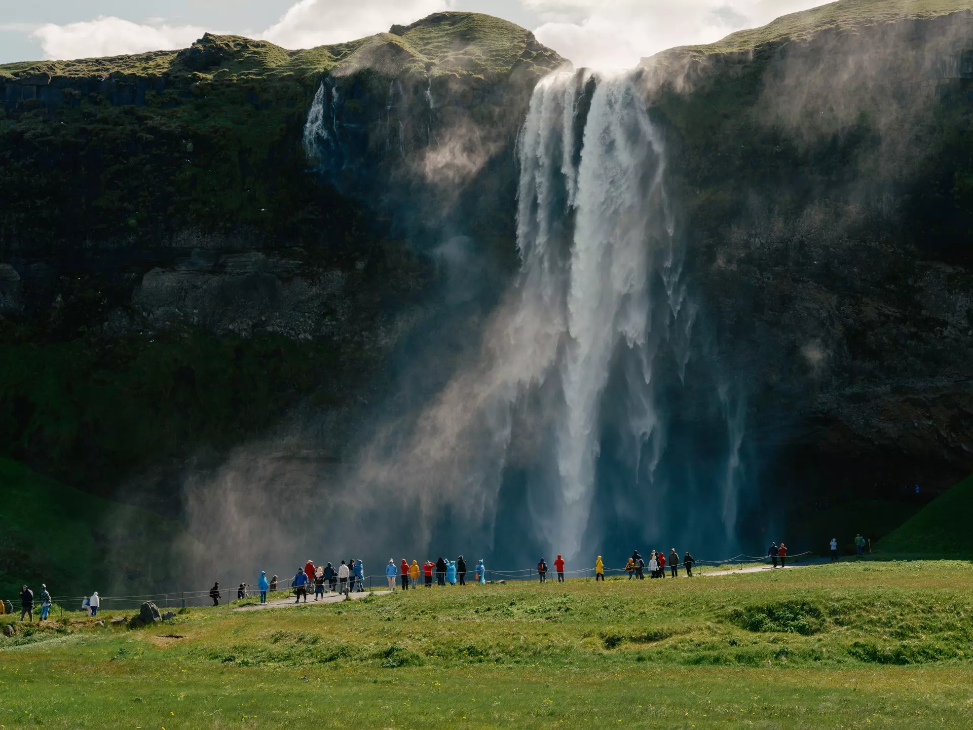 A waterfall in green hills with people below watching 