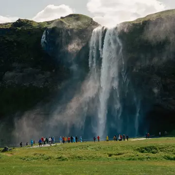 A waterfall in green hills with people below watching 