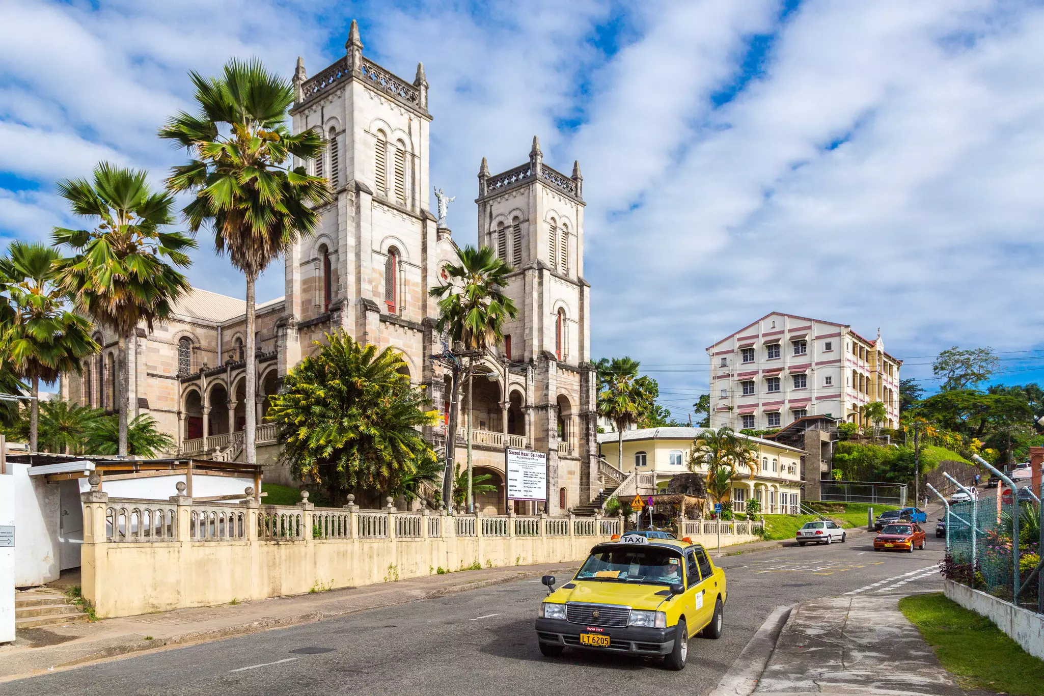 A yellow car with a sign that reads "TAXI" on the roof drives past a large cathedral.