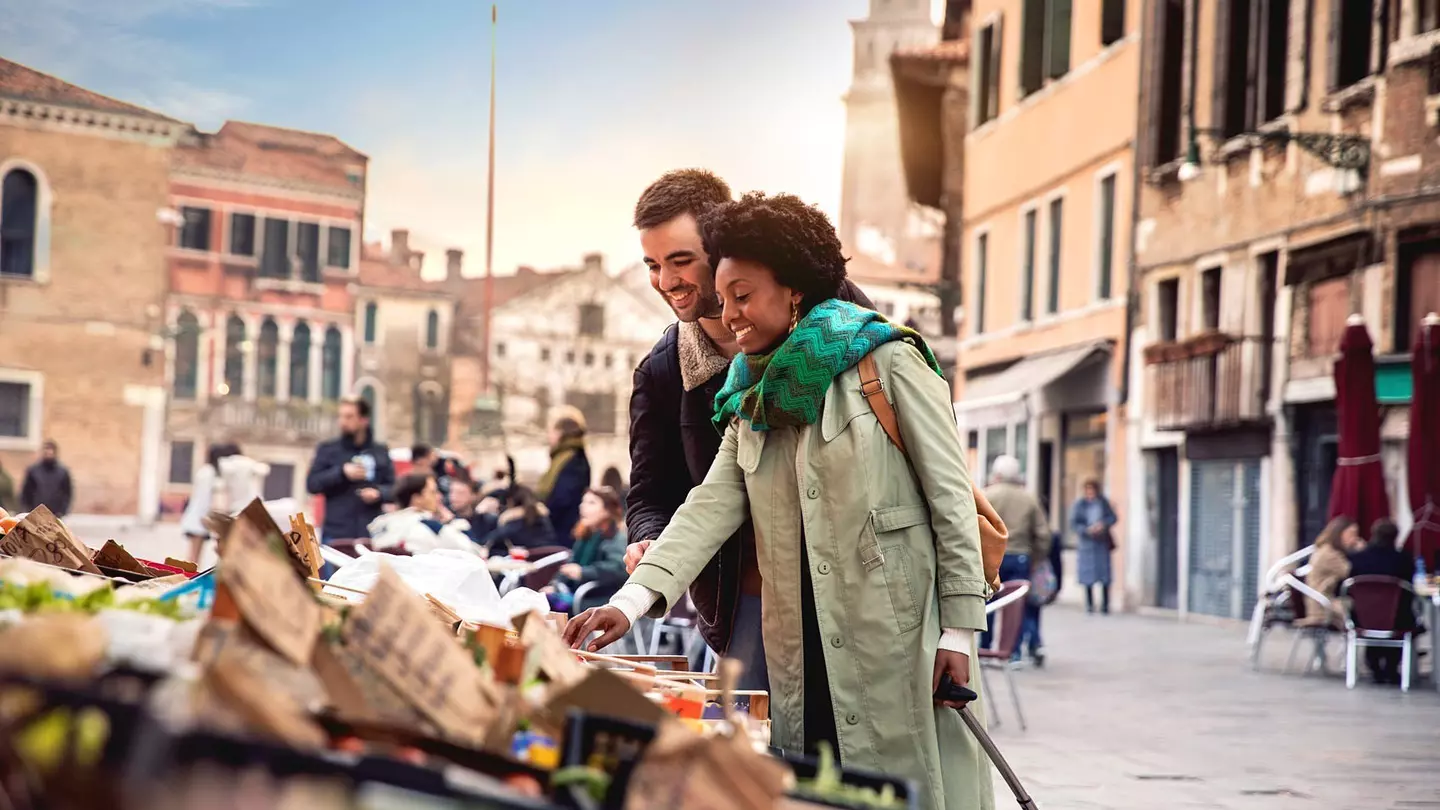 A woman and man shop at a stall in historic Venice.