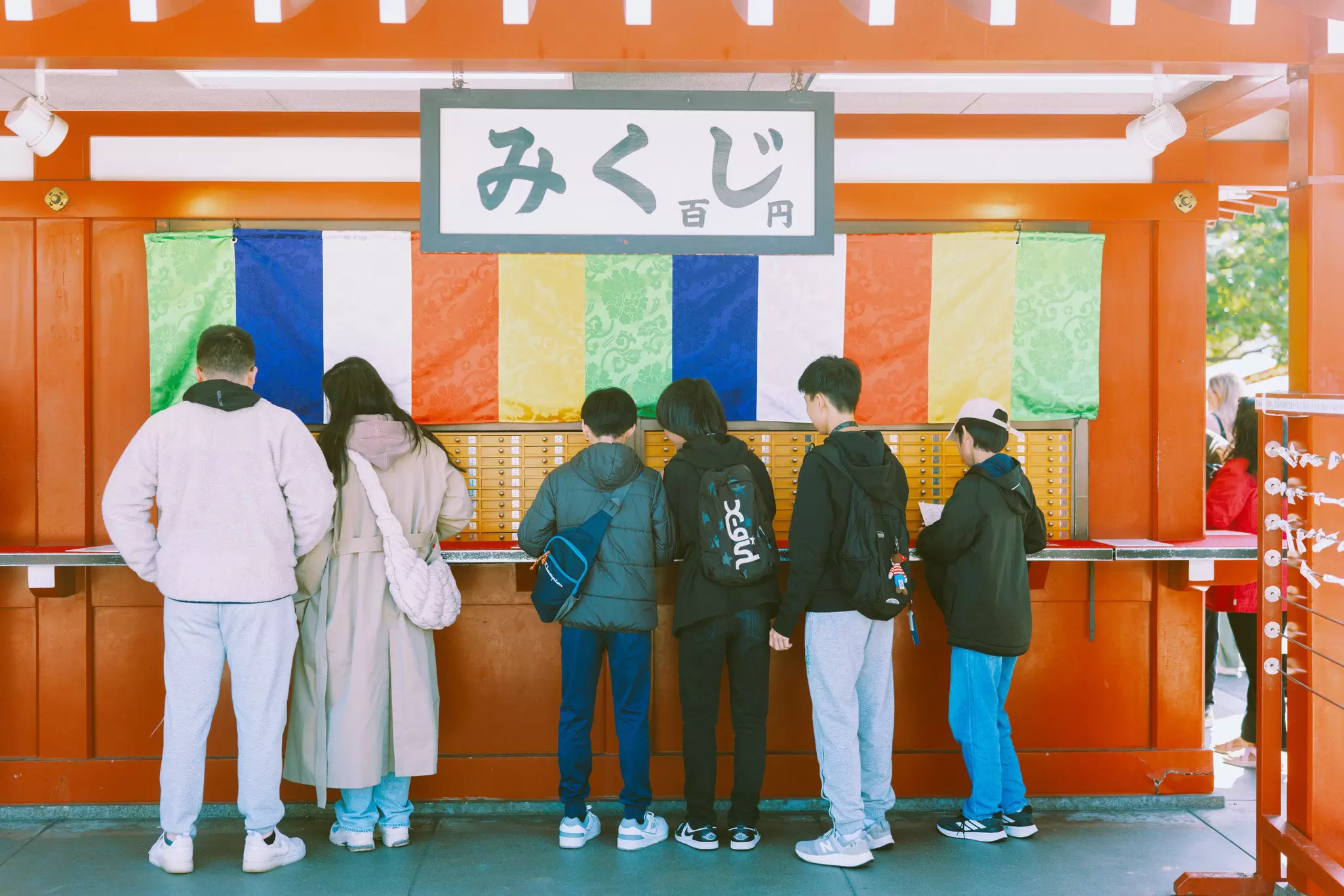 TOKYO, JAPAN. APRIL 2025. 
ASAKUSA
People standing in front of an omikuji (fortune) display.