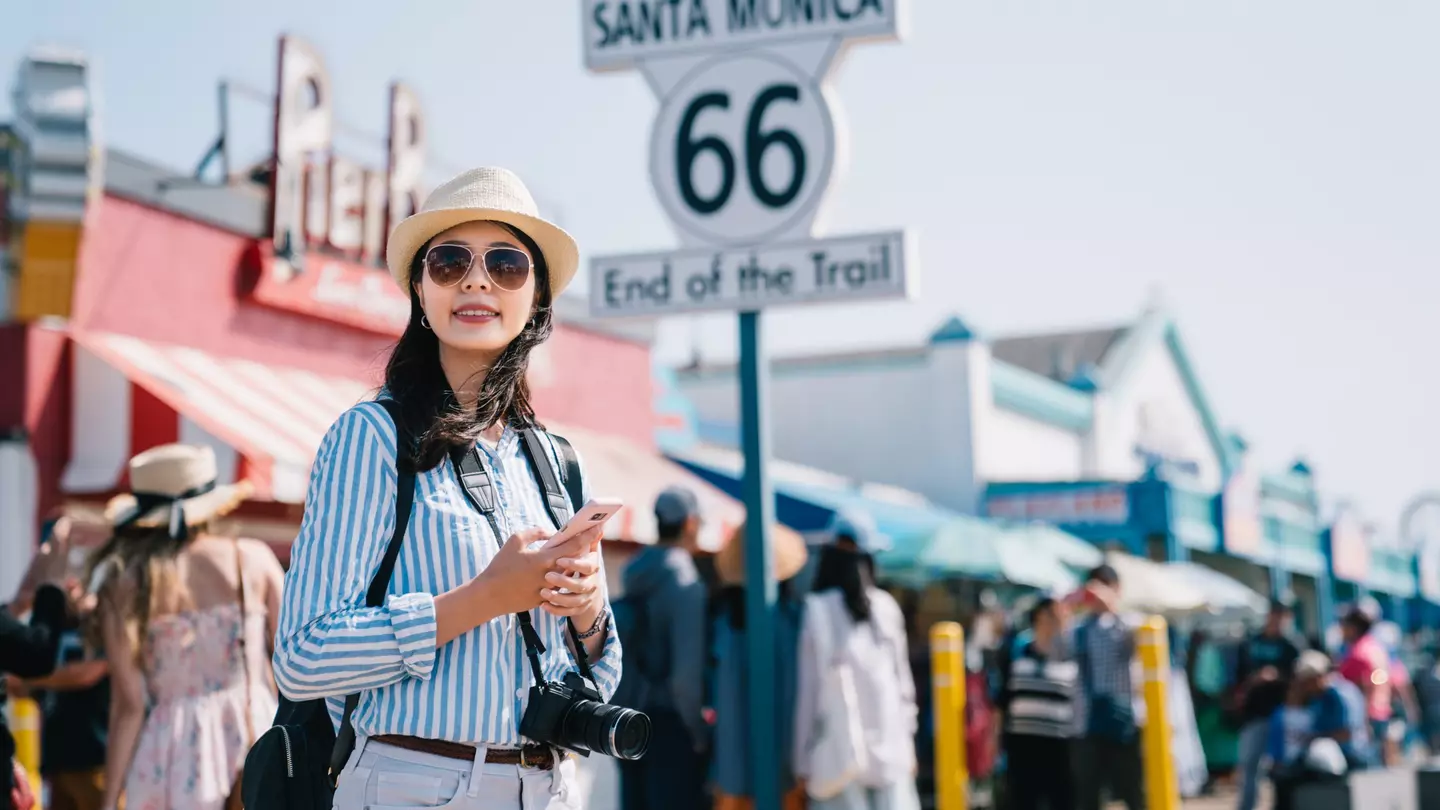A woman stands on the pier in Santa Monica near a large sign marking the end of Route 66