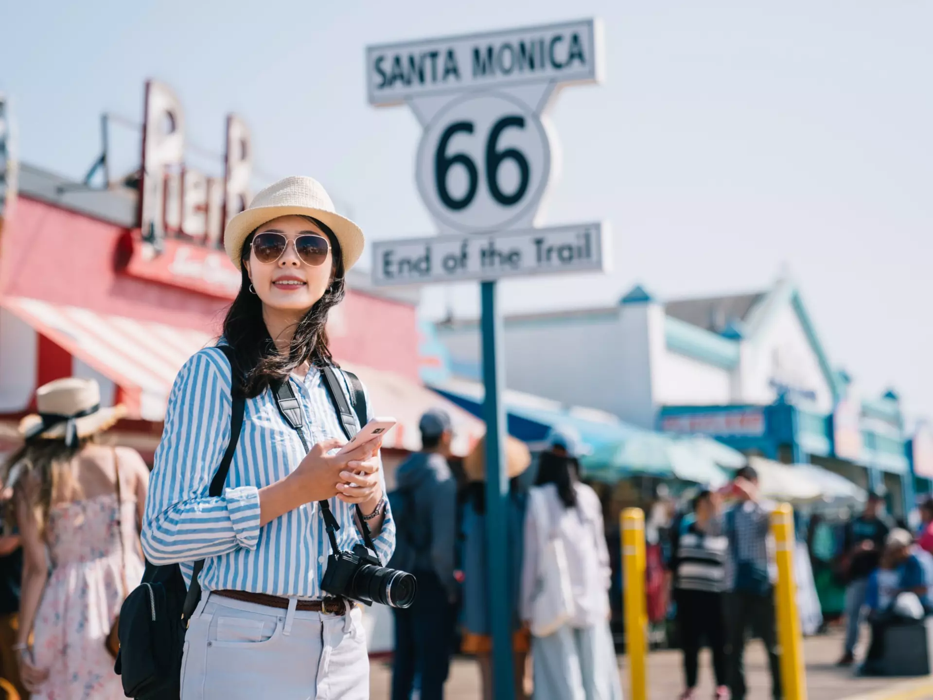 A woman stands on the pier in Santa Monica near a large sign marking the end of Route 66